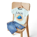 Mini & Mama light mint green graphic t-shirt with "6 GRACIAS" and blue baseball cap, paired with blue denim shorts with graphic detail.