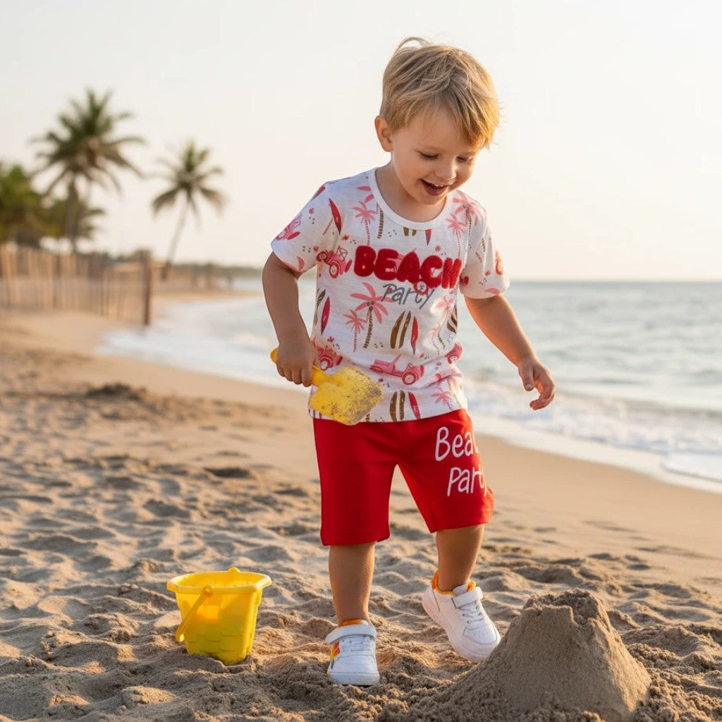 Mini & Mama white t-shirt with red "Beach Party" graphic and red shorts, worn by a boy on the beach.
